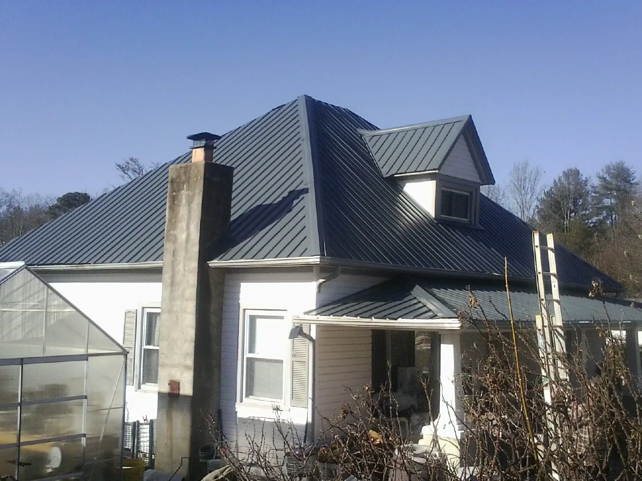 Dark blue standing seam metal roof on a white farmhouse with dormer — Slate & Tile Roof Repair by Roofing Brothers in Alloy