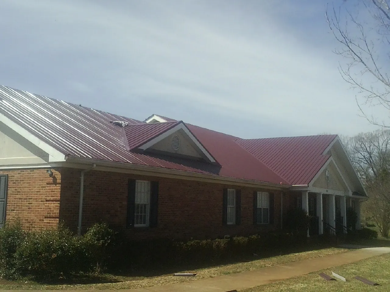Red metal roof with gabled entries on a long brick building, from a Hail Damage Roof Repair job in Alloy