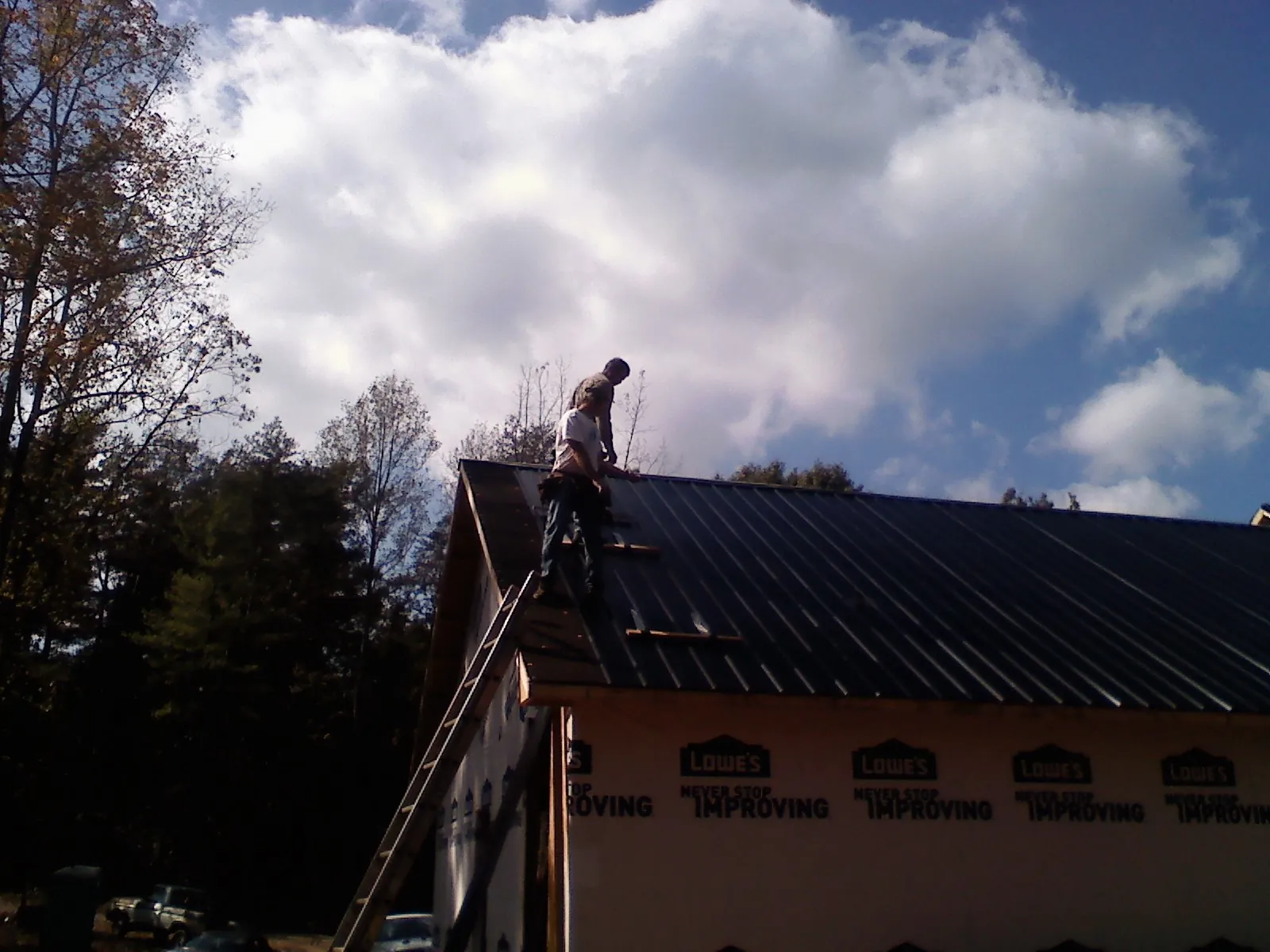 Roofer fastening dark metal panels high against a cloudy sky, from a Roof Inspection job in Alloy