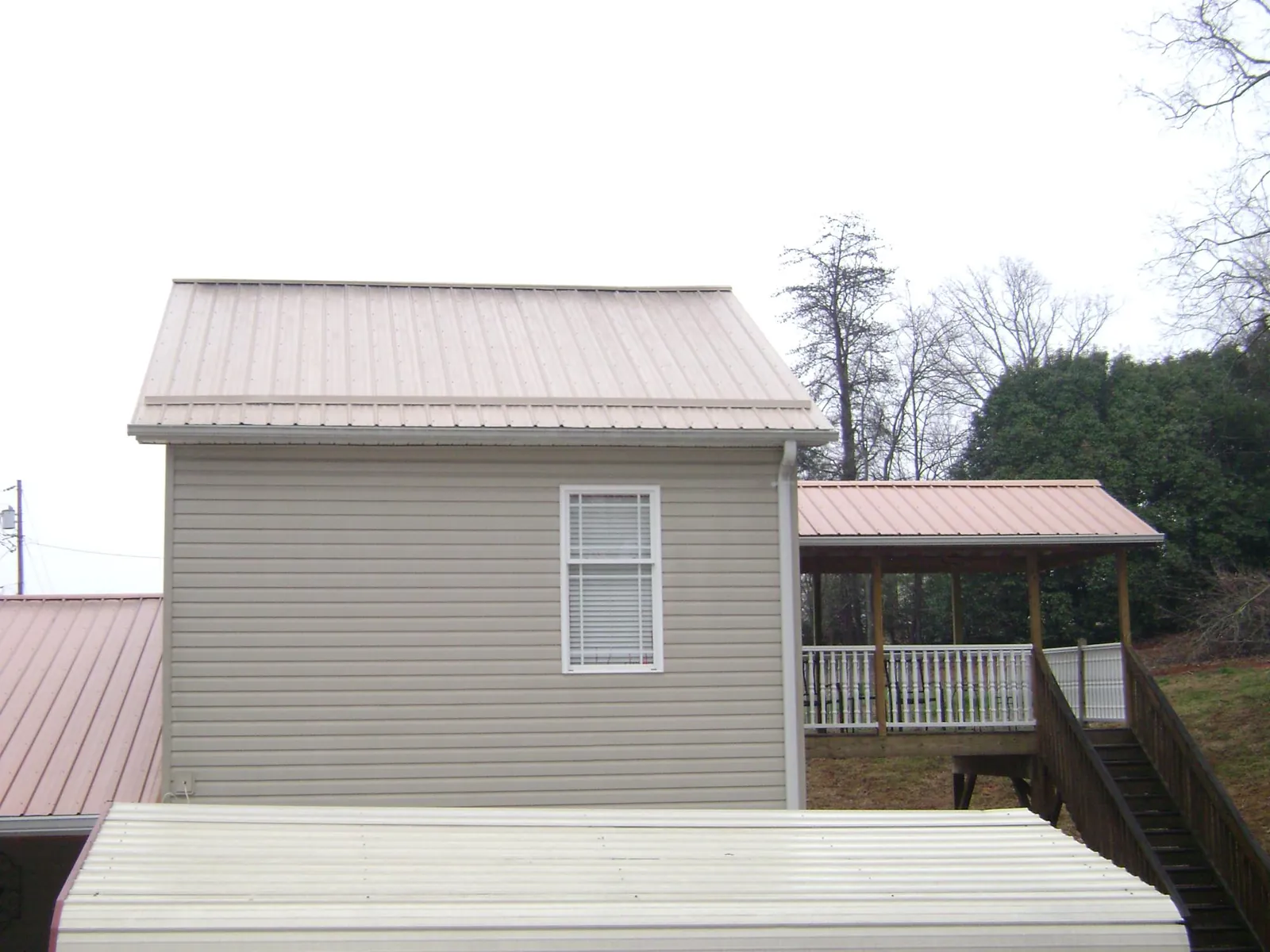 Tan metal roofs on a two story addition and attached porch, from a Roof Replacement job in Alloy